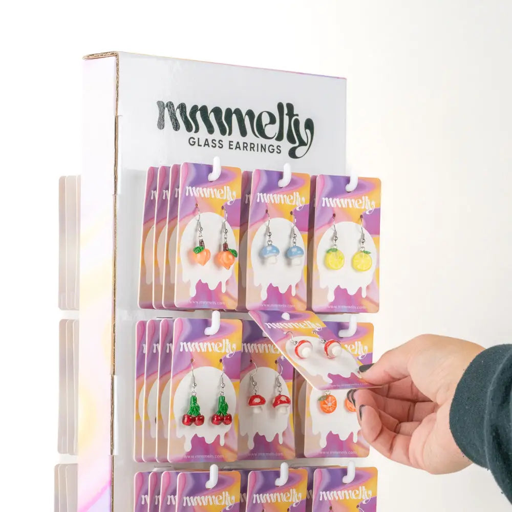 Hand holding cherry-shaped earrings in assorted earring refill kits