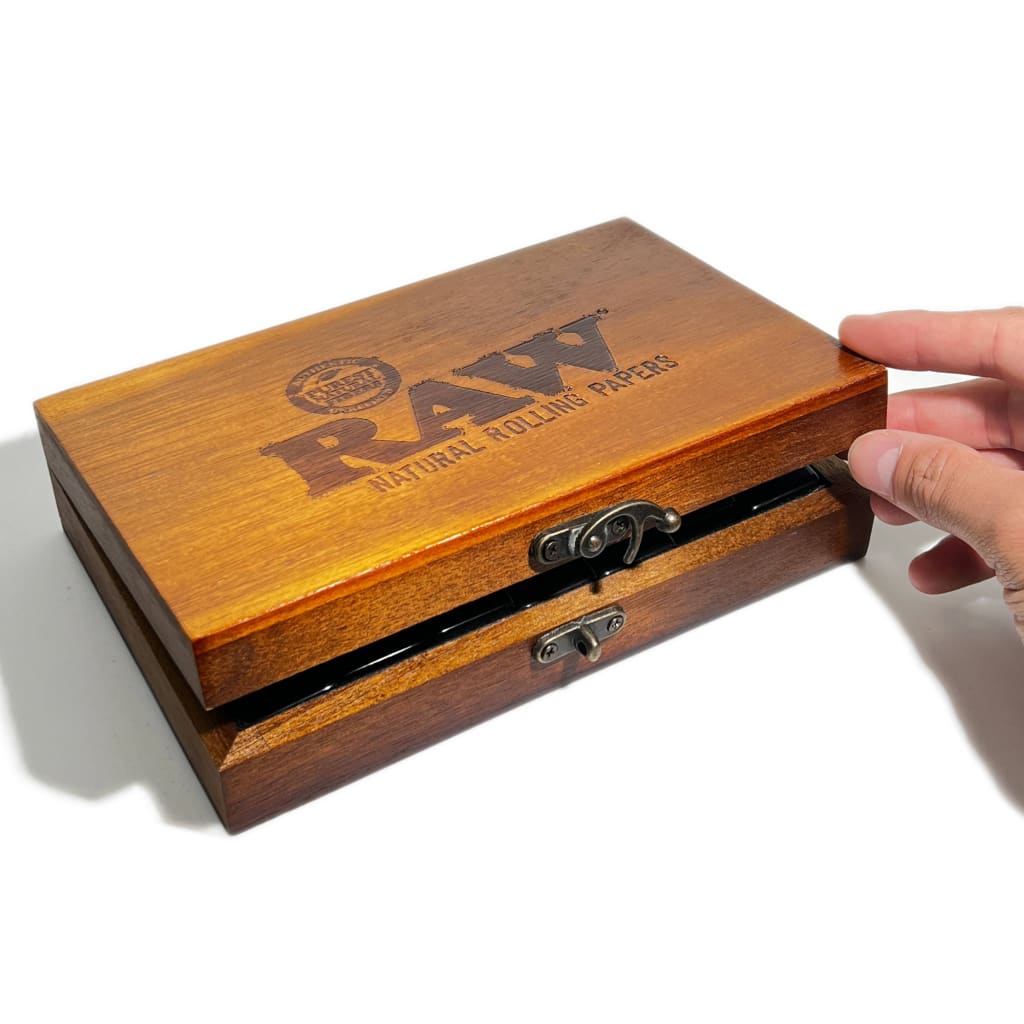 Hand opening a wooden box with ’RAW’ branding and metal latch for Raw Double Six Dominoes Set