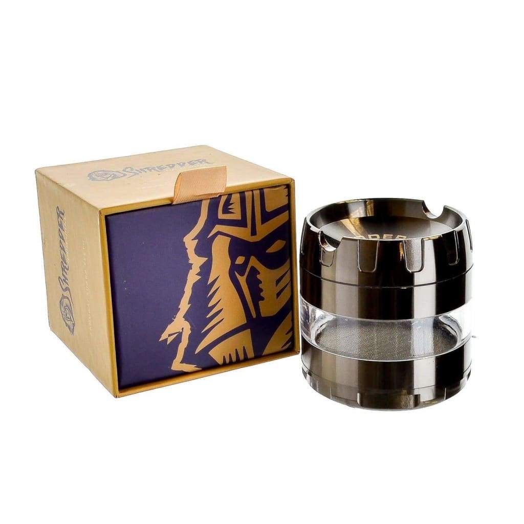 Clear glass container with black metal rings next to blue and gold box for Premium Grinder