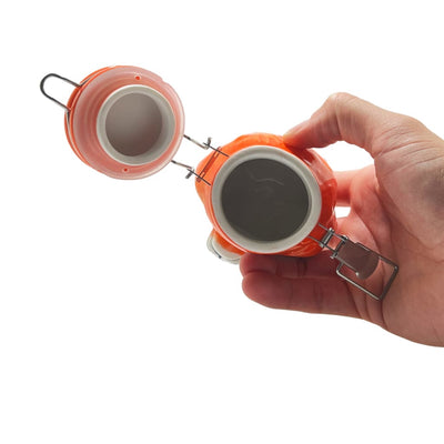 Hand holding orange ceramic storage jar with hinged lid, perfect for elegant home decor