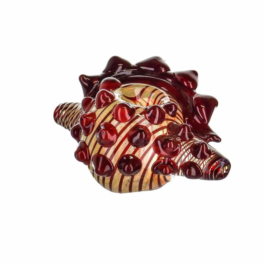 Glass hedgehog figurine with red spikes in borosilicate glass, displayed near conch shell pipe
