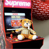 Supreme-branded arcade cabinet with Lit Plush Benny cuddly smoking buddy on control panel